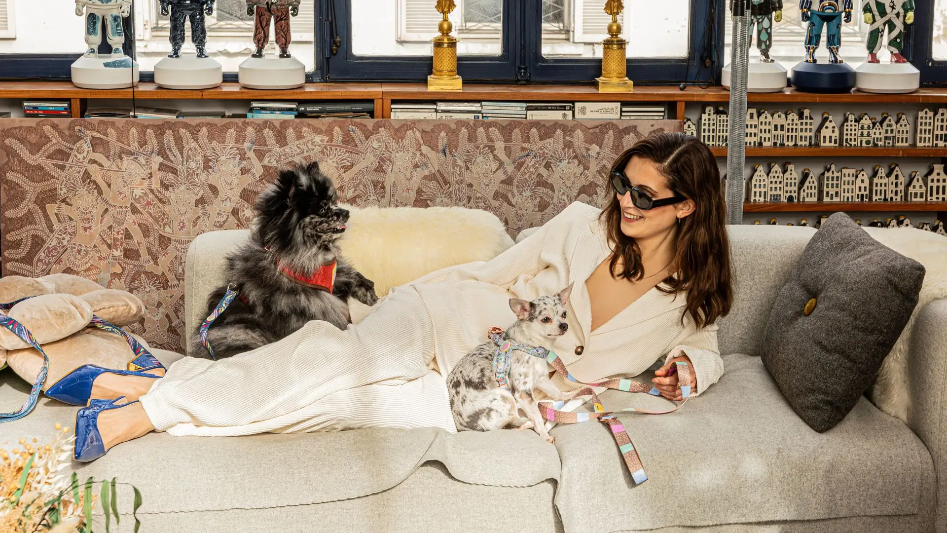 Elegant indoor scene with two dogs in Le ChouChou Paris harnesses resting beside their owner on a beige sofa.